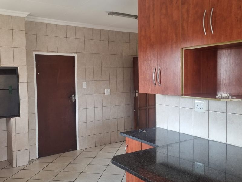 A functional kitchen featuring built-in cabinetry, granite countertops, tiled walls, and a built-in indoor braai area.