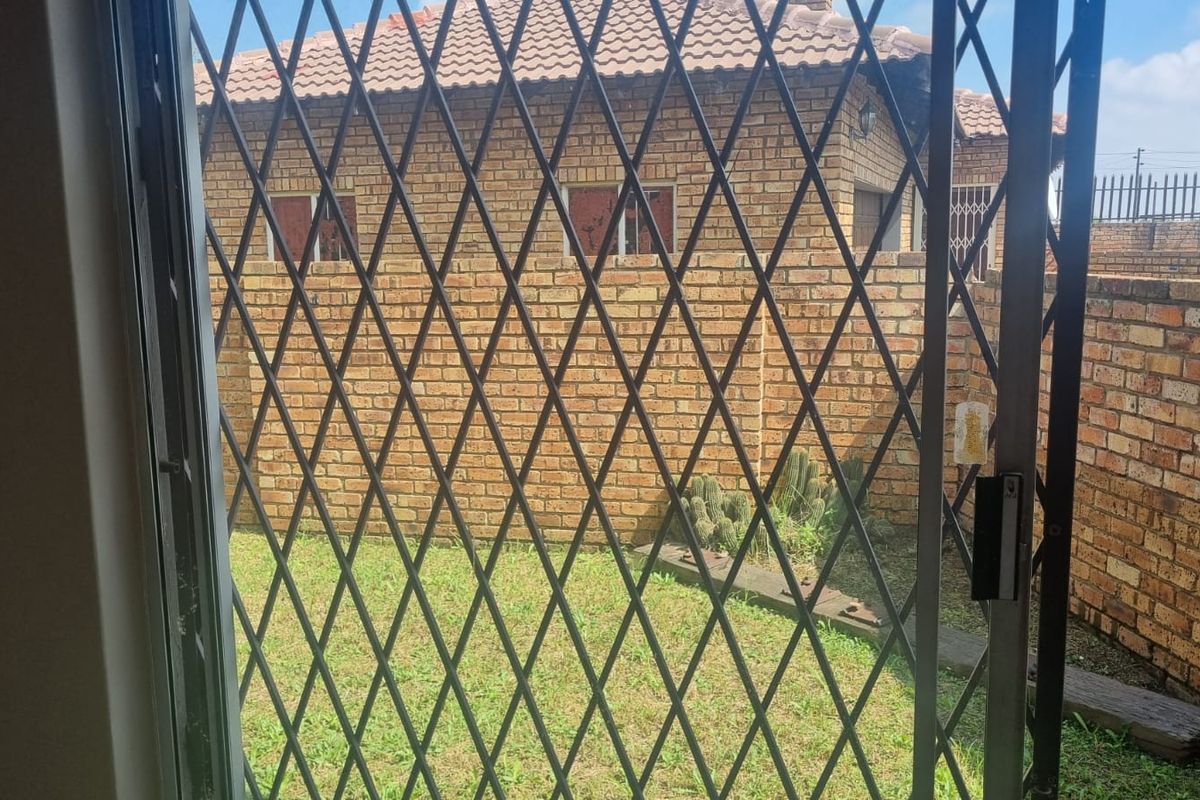 View of the rear garden and brick exterior wall from inside, featuring a security gate and sliding door access.