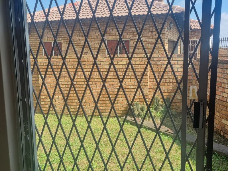 View of the rear garden and brick exterior wall from inside, featuring a security gate and sliding door access.