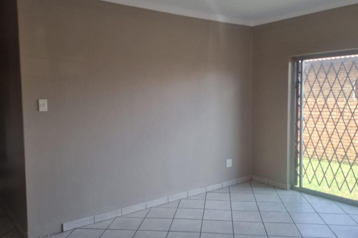 An empty living room featuring neutral wall paint, tiled flooring, and a sliding glass door with a security gate leading to the exterior.