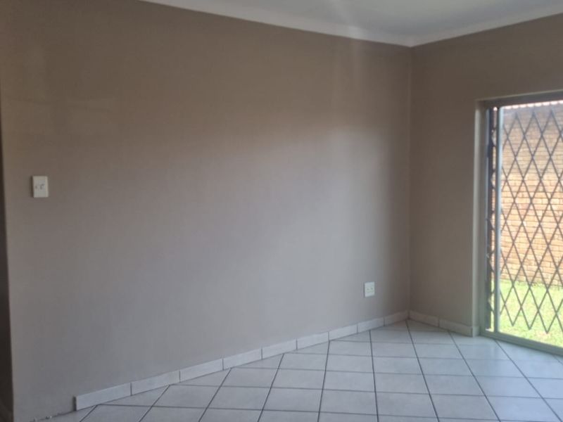 An empty living room featuring neutral wall paint, tiled flooring, and a sliding glass door with a security gate leading to the exterior.