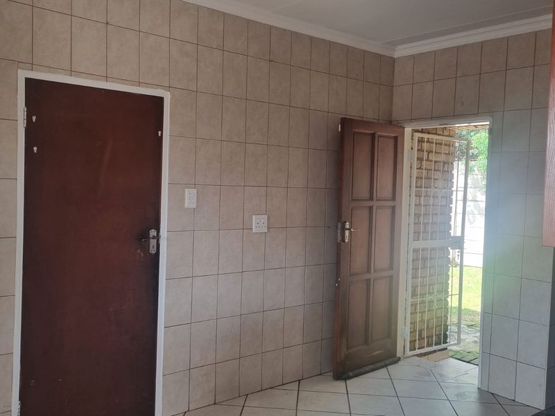 A functional kitchen area featuring tiled walls and flooring, with direct access to the exterior through a wooden door and security gate.