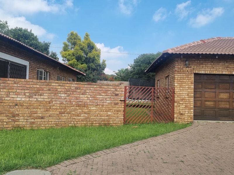 Front exterior view of a face brick townhouse featuring a paved driveway, garage, and perimeter boundary wall with a metal gate.