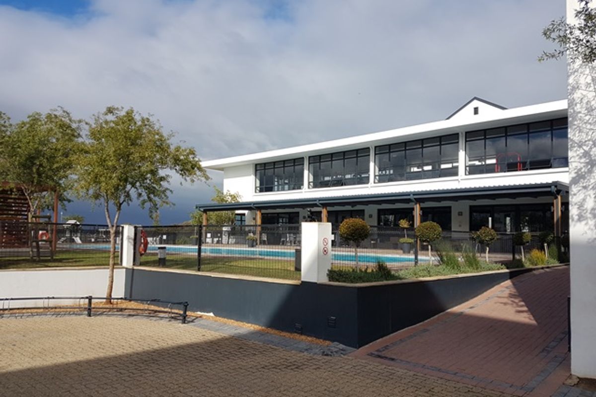 Exterior view of a modern apartment complex featuring a swimming pool, paved driveway, and a covered patio area with large windows.
