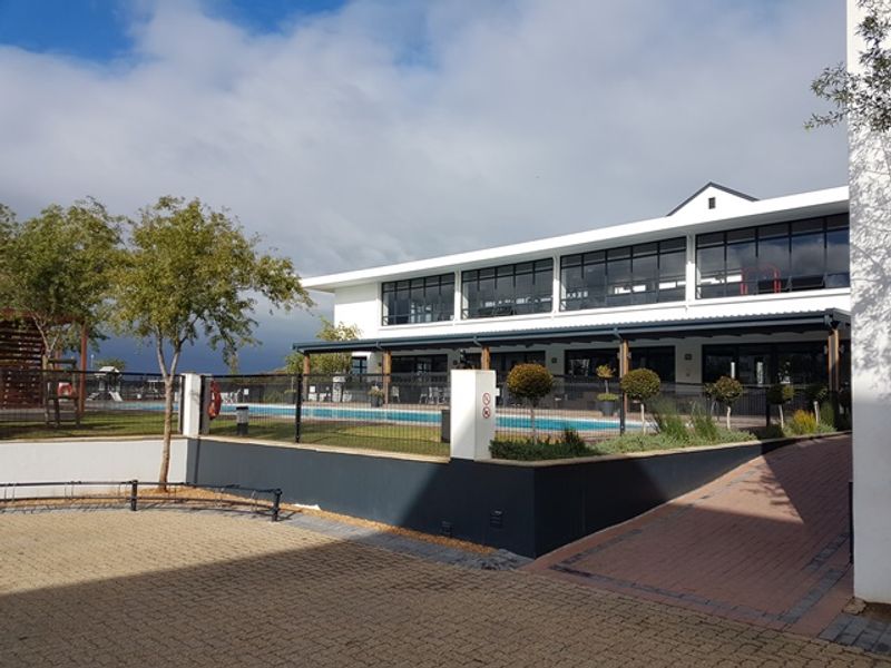 Exterior view of a modern apartment complex featuring a swimming pool, paved driveway, and a covered patio area with large windows.