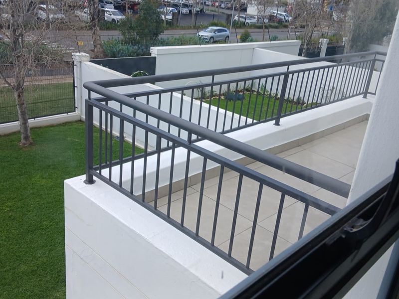 An elevated balcony featuring a metal balustrade and tiled flooring, overlooking a private garden area and street view.