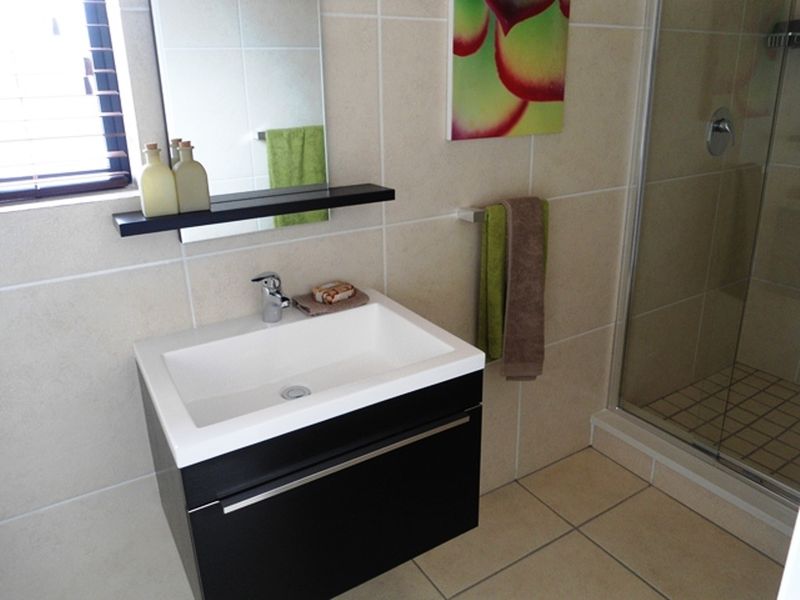 A modern bathroom featuring a sleek black vanity cabinet, ceramic basin, wall-mounted mirror, and a glass-enclosed shower with neutral wall and floor tiling.