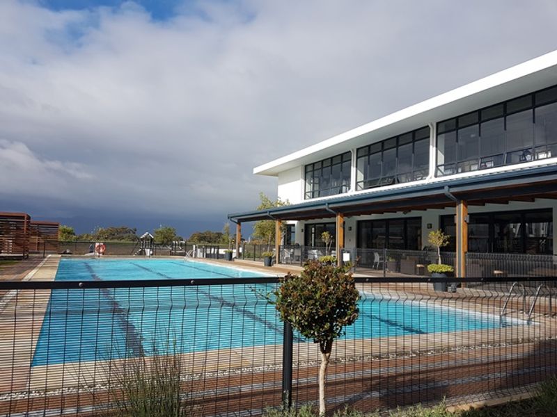 A well-maintained communal swimming pool area featuring timber decking, a covered patio, and modern building architecture with large glass windows.