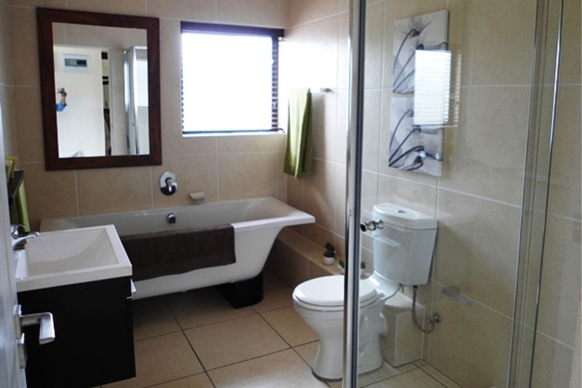 A well-maintained bathroom featuring a freestanding bathtub, a separate glass-enclosed shower, a wall-mounted vanity, and neutral ceramic tiling throughout.