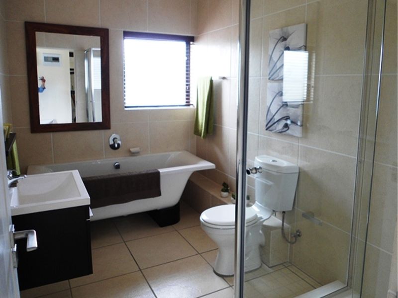 A well-maintained bathroom featuring a freestanding bathtub, a separate glass-enclosed shower, a wall-mounted vanity, and neutral ceramic tiling throughout.