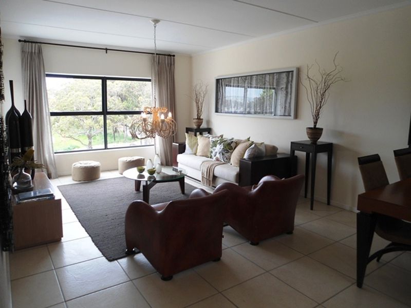 Spacious open-plan living area featuring neutral tiled flooring, large windows providing natural light, and a contemporary ceiling light fixture.