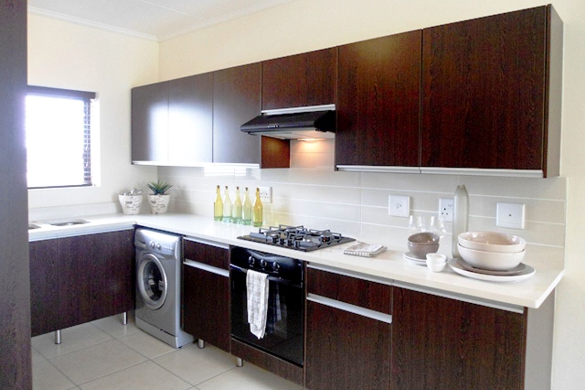 Modern kitchen featuring dark wood cabinetry, white stone countertops, built-in gas hob, oven, extractor fan, and integrated washing machine with tiled flooring.