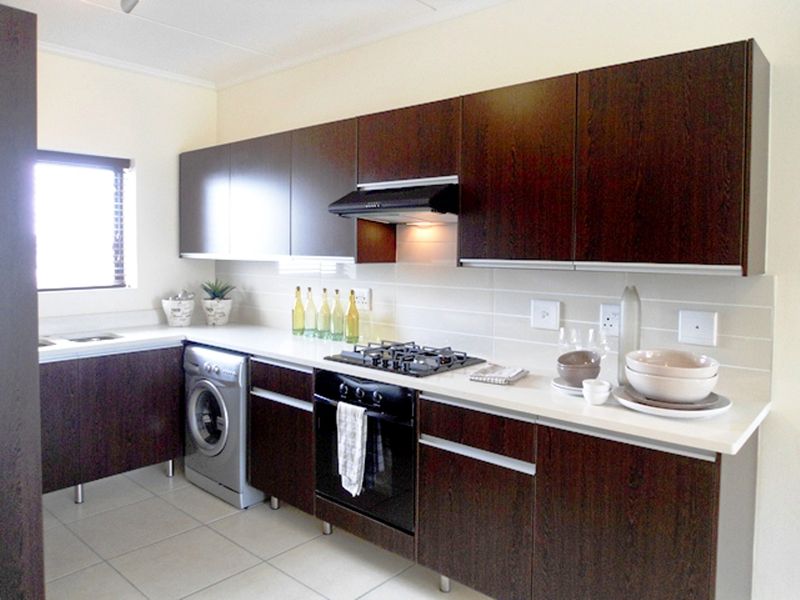 Modern kitchen featuring dark wood cabinetry, white stone countertops, built-in gas hob, oven, extractor fan, and integrated washing machine with tiled flooring.