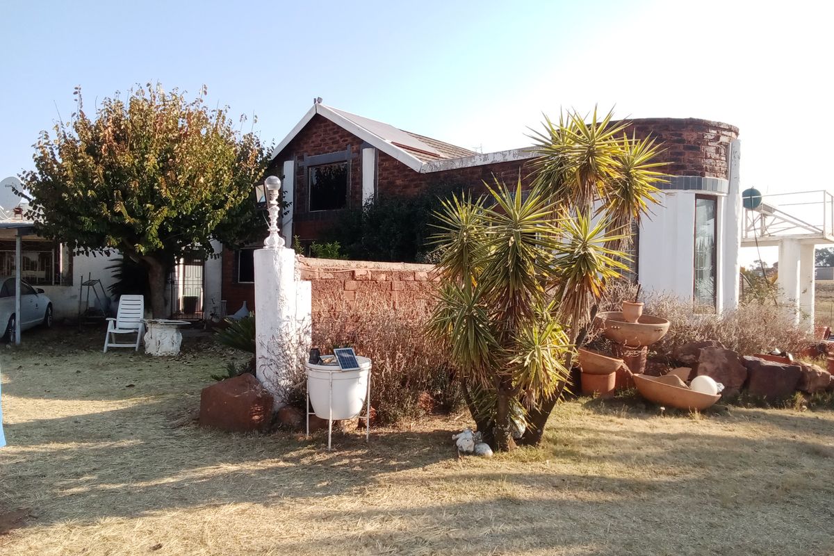 Rear view of a farm property featuring a brick facade, metal roofing, and a surrounding garden area with established landscaping.