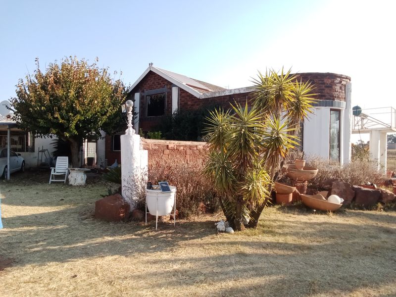 Rear view of a farm property featuring a brick facade, metal roofing, and a surrounding garden area with established landscaping.