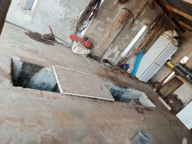 A rustic garage space featuring a concrete floor with a built-in inspection pit, showing significant wear and requiring maintenance or renovation.