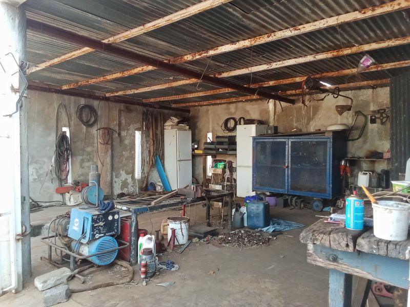 A functional farm utility space or workshop featuring a corrugated metal roof, exposed steel beams, and concrete flooring, suitable for storage or maintenance tasks.