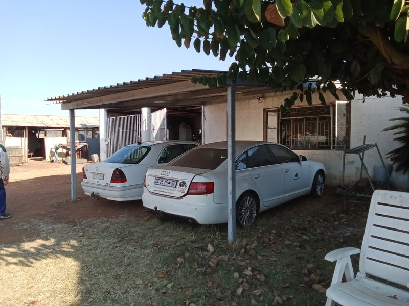 Rear exterior view of the farm property featuring a corrugated metal carport structure attached to the main building with visible security window bars.