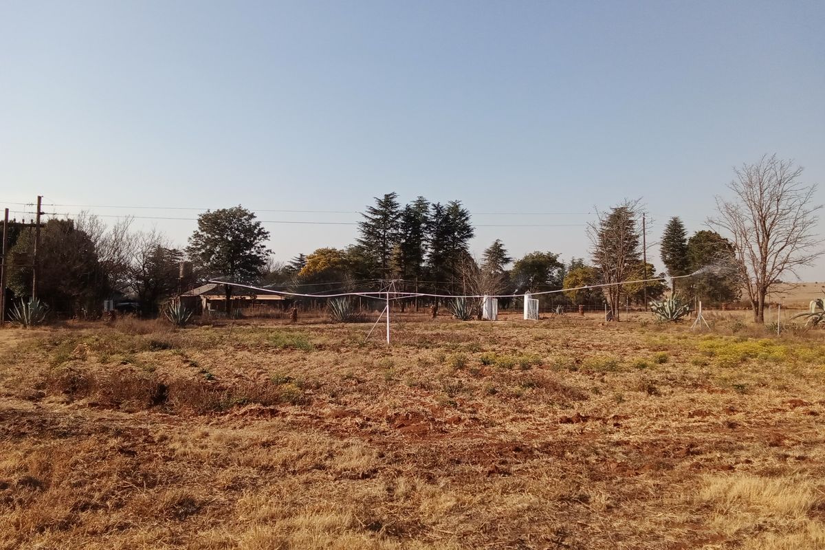 An open farm field featuring an active overhead irrigation system and mature trees in the background.