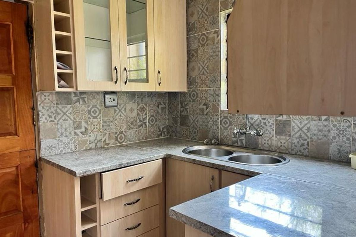 A functional kitchen area featuring light wood-tone cabinetry, patterned wall tiling, and a double-bowl stainless steel sink with a mixer tap.