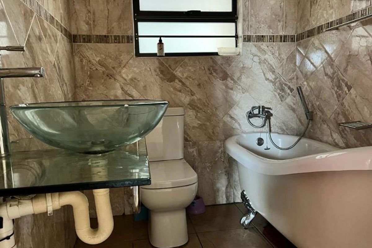 A bathroom featuring a clawfoot bathtub, glass vessel sink, and full-height wall tiling with a decorative border.