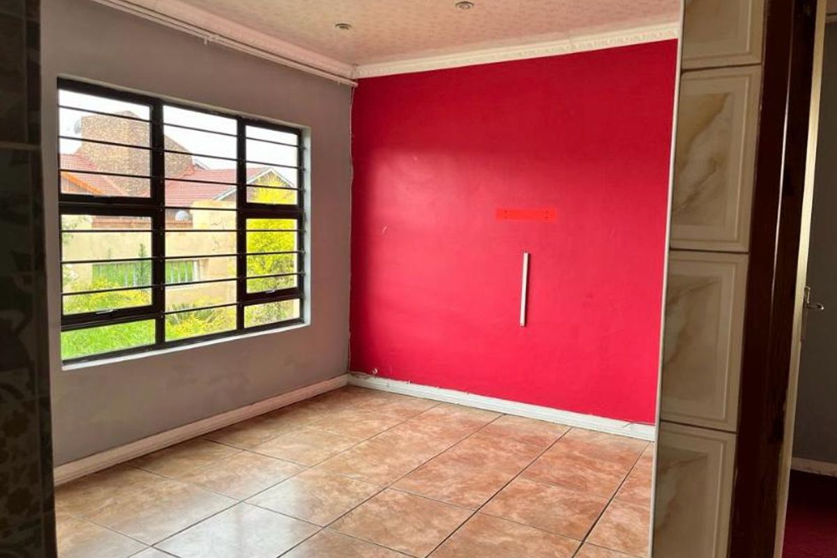 An empty bedroom featuring tiled flooring, security bars on the window, and built-in cupboard storage, ready for a fresh update.