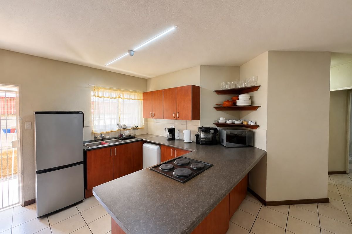 Functional kitchen featuring wood-finish cabinetry, laminate countertops, an integrated electric hob, and tiled flooring with direct access to an exterior area.