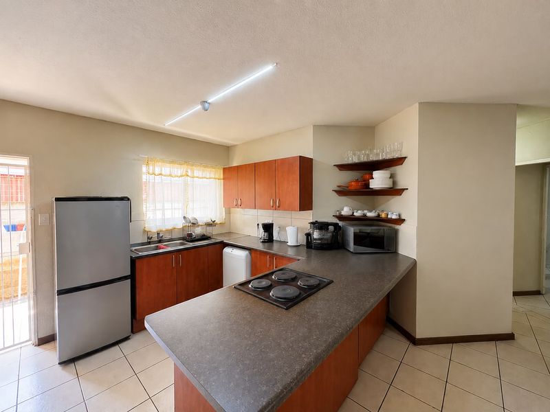 Functional kitchen featuring wood-finish cabinetry, laminate countertops, an integrated electric hob, and tiled flooring with direct access to an exterior area.