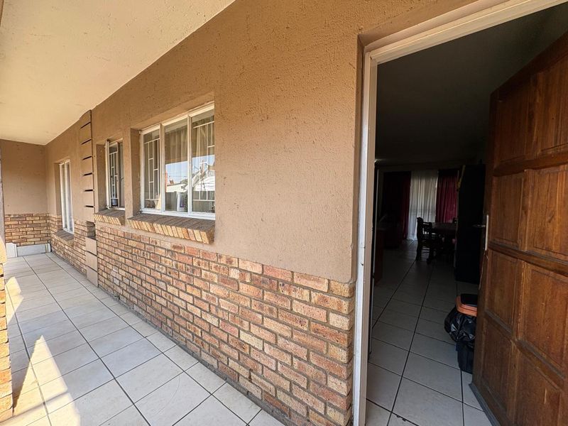 A covered patio area featuring tiled flooring and a brick facade, providing direct access to the interior living space through a timber door.