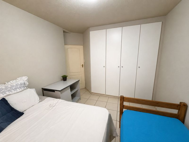 A functional bedroom featuring tiled flooring and ample built-in cupboard storage space.
