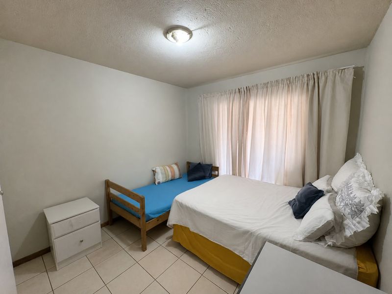 A functional bedroom featuring tiled flooring and a ceiling-mounted light fixture, offering a neutral space ready for personalization.