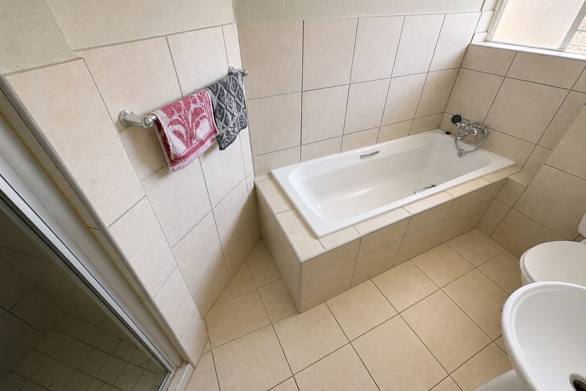 A clean, functional bathroom featuring a built-in bathtub, tiled walls and flooring, a pedestal basin, and a separate shower enclosure.
