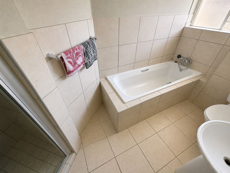 A clean, functional bathroom featuring a built-in bathtub, tiled walls and flooring, a pedestal basin, and a separate shower enclosure.