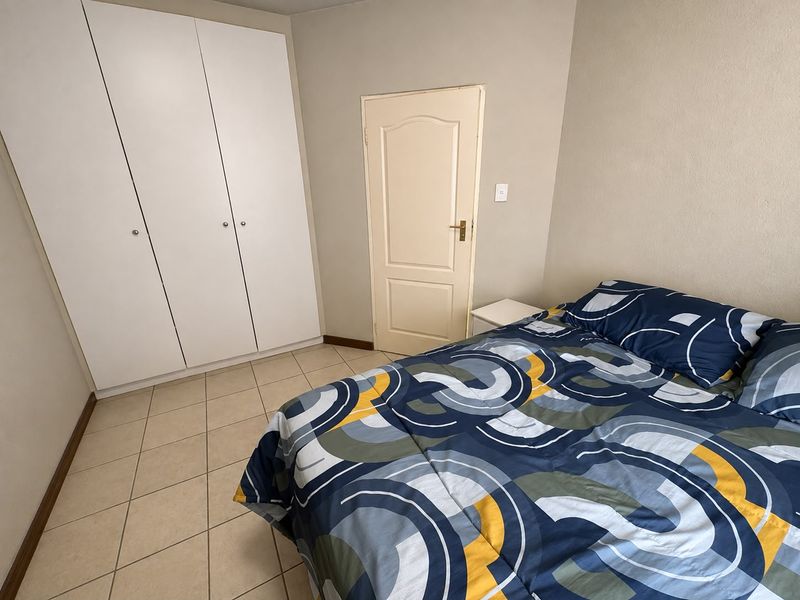 A functional bedroom featuring neutral wall tones, tiled flooring, and built-in storage cupboards.