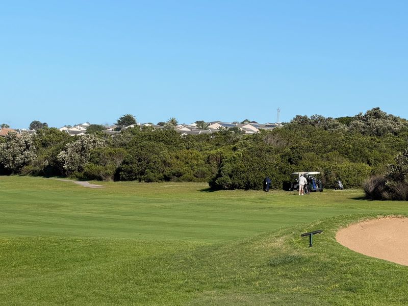 A scenic view overlooking a well-maintained golf course fairway with a sand bunker and surrounding natural vegetation.