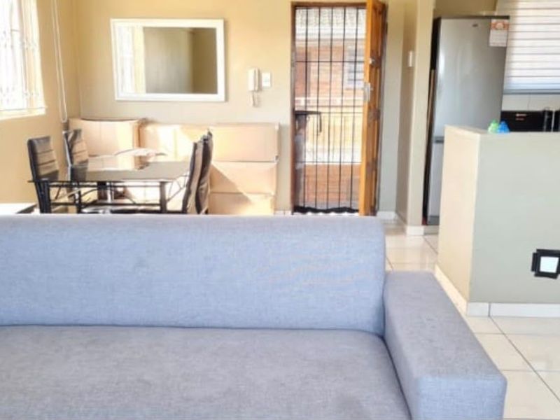 Open plan living and dining area featuring tiled flooring, security bars on windows, and a security gate leading to the exterior.