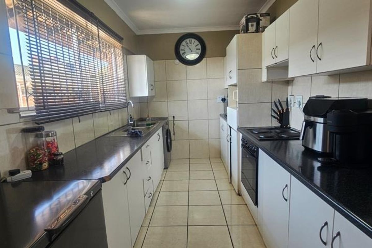 A functional galley-style kitchen featuring white cabinetry, dark laminate countertops, built-in oven, electric hob, and tiled finishes throughout.