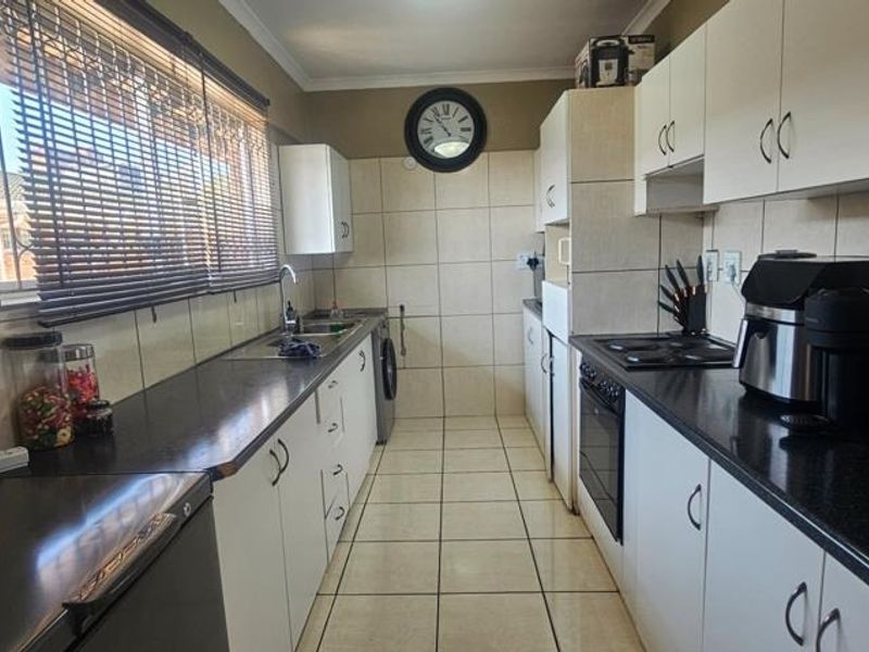 A functional galley-style kitchen featuring white cabinetry, dark laminate countertops, built-in oven, electric hob, and tiled finishes throughout.