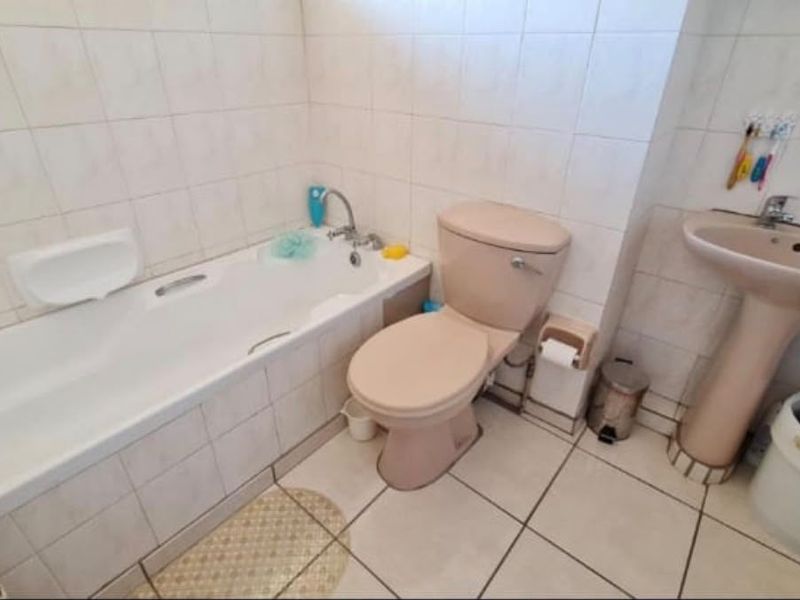 A dated bathroom featuring a pastel-colored suite, including a bathtub, pedestal sink, and toilet, finished with neutral ceramic wall and floor tiles.