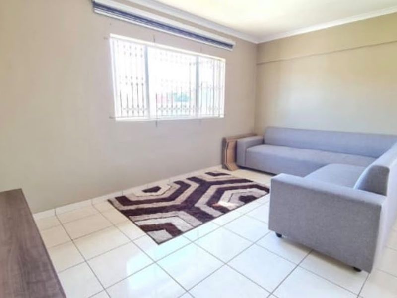 A functional living room featuring neutral wall tones, tiled flooring, and a window fitted with security bars.