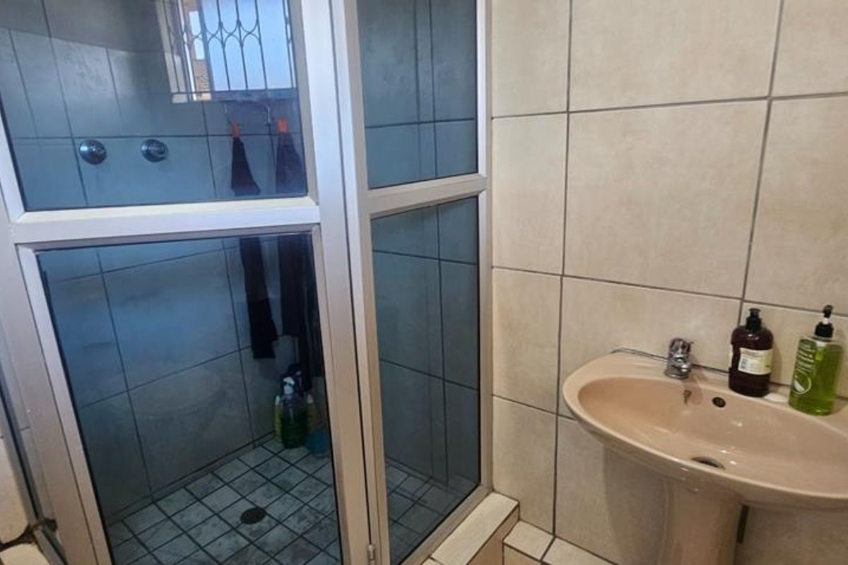A functional bathroom featuring a pedestal basin and a glass-enclosed shower with neutral wall and floor tiling.
