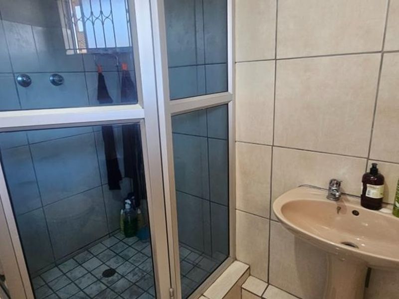 A functional bathroom featuring a pedestal basin and a glass-enclosed shower with neutral wall and floor tiling.
