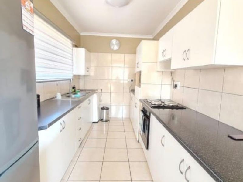 A functional galley-style kitchen featuring white cabinetry, dark laminate countertops, tiled backsplash, and built-in cooking appliances.