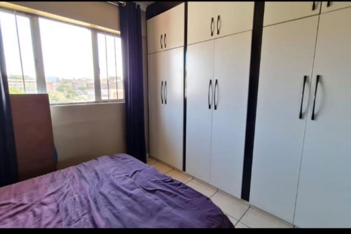 A bedroom featuring built-in cupboards and tiled flooring, offering functional storage space and natural light from the window.