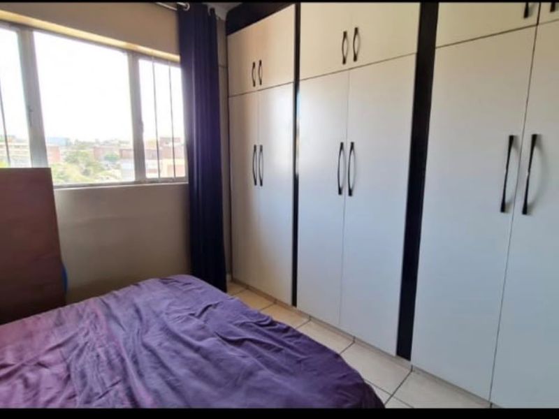 A bedroom featuring built-in cupboards and tiled flooring, offering functional storage space and natural light from the window.
