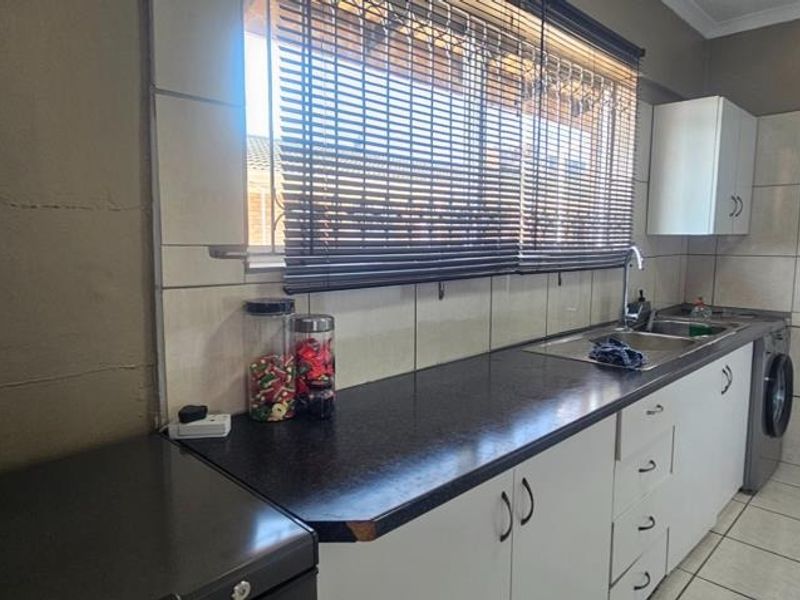 A functional kitchen featuring laminate countertops, built-in cabinetry, a stainless steel sink, and tiled finishes throughout.