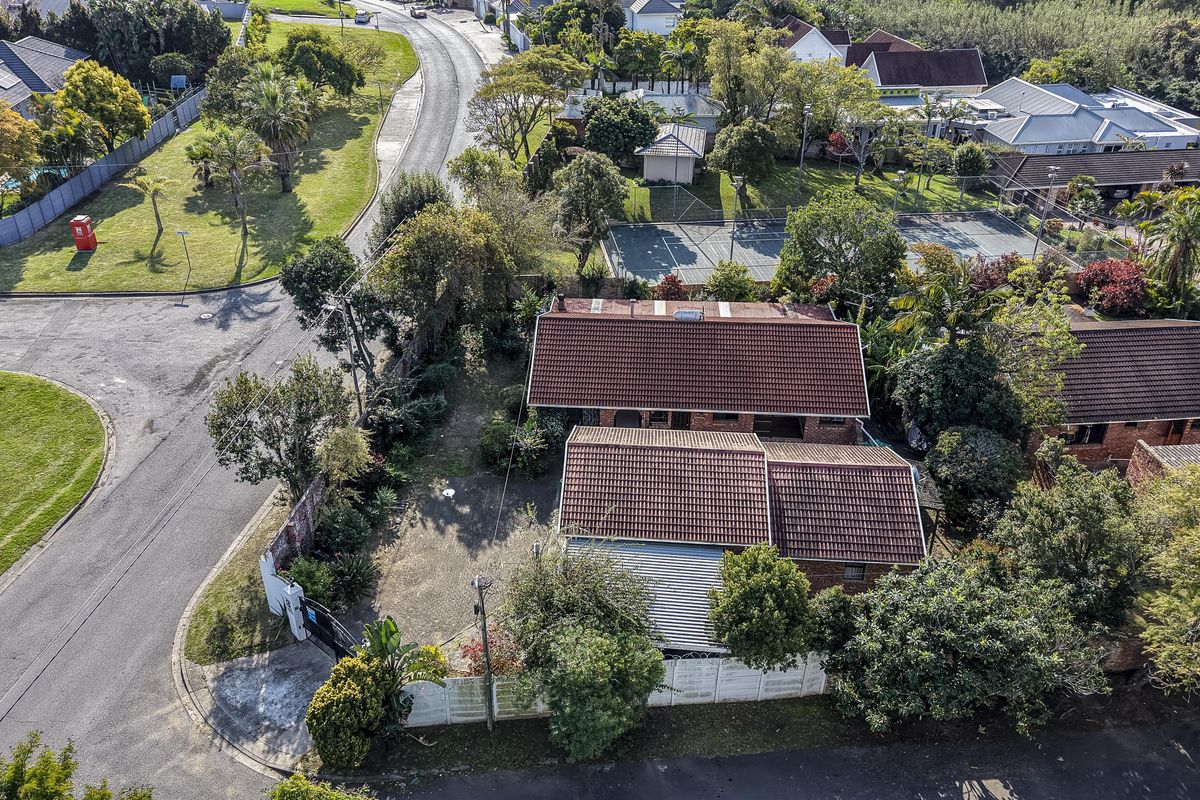 Aerial view of a residential property featuring a tiled roof, brick exterior, and a gated driveway within a suburban neighborhood setting.