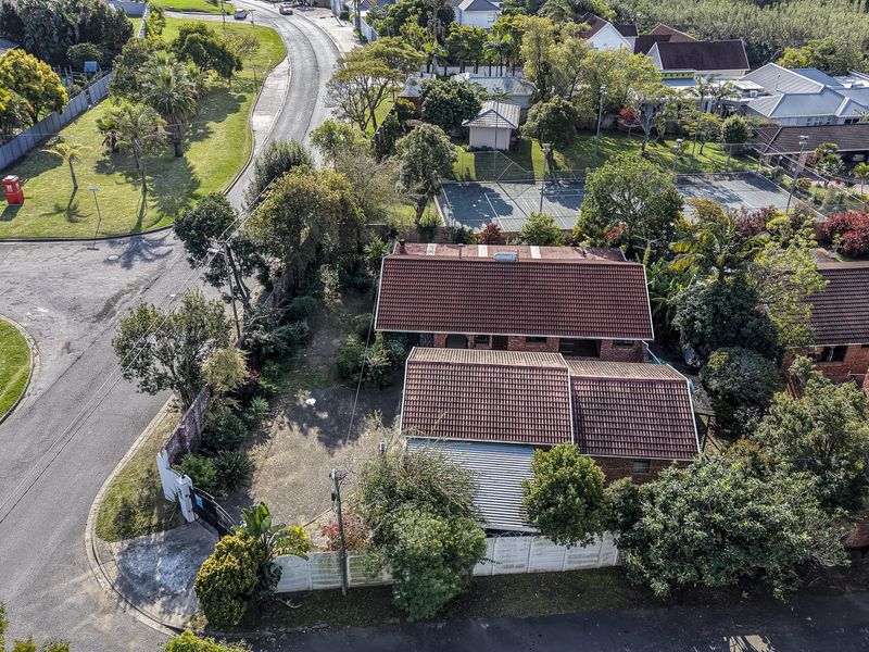 Aerial view of a residential property featuring a tiled roof, brick exterior, and a gated driveway within a suburban neighborhood setting.