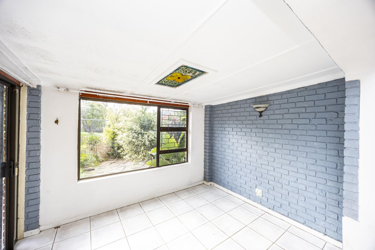 An empty living area featuring a painted brick feature wall, tiled flooring, and a large window overlooking the garden.