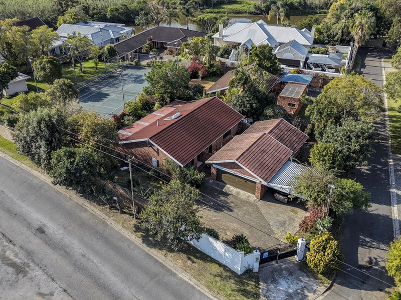 Aerial view of a residential property featuring a tiled roof house, garage, carport, paved driveway, and access to a shared tennis court.